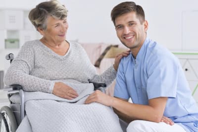 image of senior woman on a wheelchair and smiling male caregiver